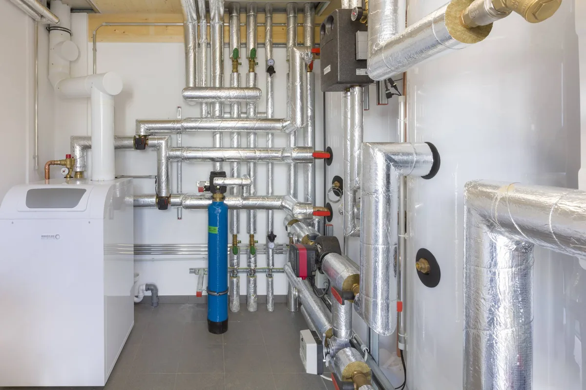Technikraum mit verzweigten Edelstahl-Versorgungsleitungen, gedämmten Speichern und blauer Enthärtungsanlage
